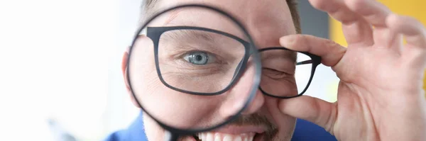 Jongeman glimlachen en houden vergrootglas voor zijn ogen close-up — Stockfoto