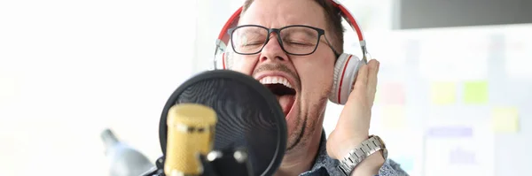 Hombre joven en auriculares cantando en el micrófono — Foto de Stock