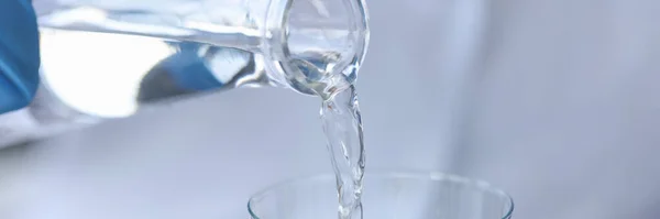 Pure water is poured from a bottle into transparent glass — 图库照片