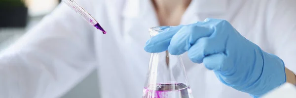 Scientist in laboratory holds transparent flask of liquid and digs purple reagent into it — Fotografia de Stock