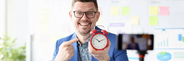 Portrait of smiling businessman holding red alarm clock in his hand — Stock Fotó