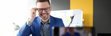 İş adamı gülümsüyor ve cep telefonu kamerasının önünde gözlükleri ayarlıyor.