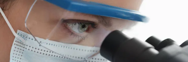 Femme chimiste en lunettes et masque regardant à travers microscope gros plan — Photo