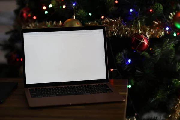 Laptop con schermo bianco vuoto su dietro è l'albero di Natale con ghirlanda — Foto Stock
