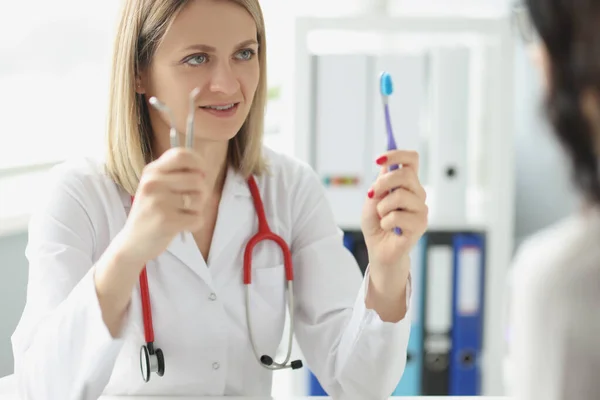 Kvinna läkare tandläkare visar patienten tandborste och dentala instrument — Stockfoto