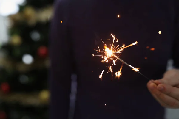 Mann hält brennende Wunderkerze in dunklen Raum vor Kulisse des Weihnachtsbaums — Stockfoto