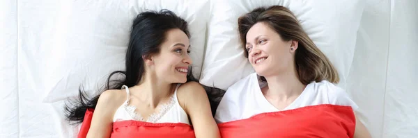 Две улыбающиеся женщины лежат на кровати с флагом lgbt — стоковое фото