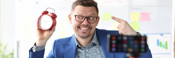 Smiling businessman holds red alarm clock and conducts online time management courses — Stock Photo, Image