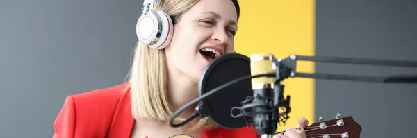 Женщина поет и играет на гитаре с наушниками перед микрофоном — стоковое фото