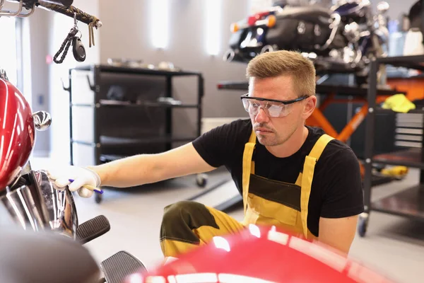 Gözlüklü bir tamirci araba tamirhanesinde motosiklete boya topluyor. — Stok fotoğraf