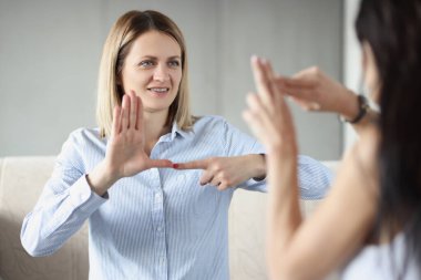 İki genç ve mutlu kadın kanepede oturup işaret dili yapıyor.