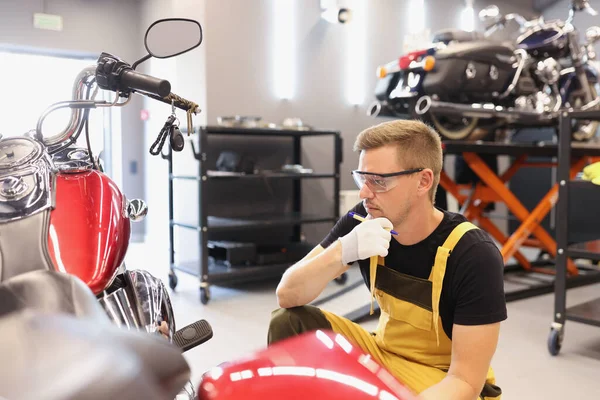 Pensive locksmith inspects the technical condition of motorcycle in workshop — 스톡 사진