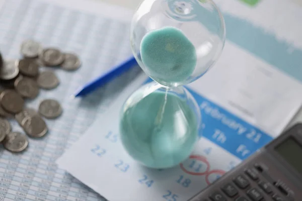Hourglass calendar and coins lie on table closeup