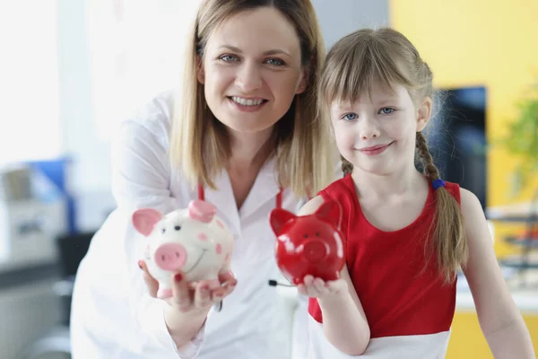 Médico pediatra y niña están sosteniendo alcancía de cerdo —  Fotos de Stock