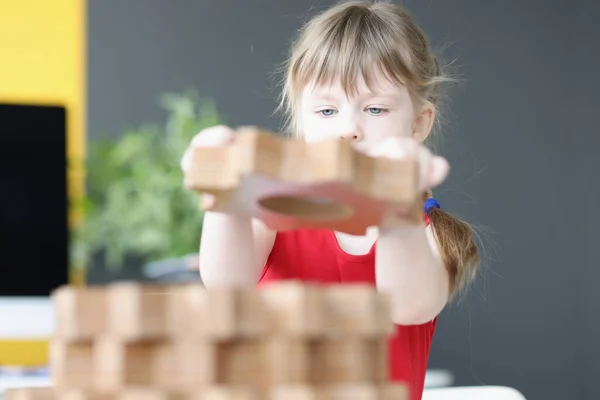 Little girl folds wooden gears on table