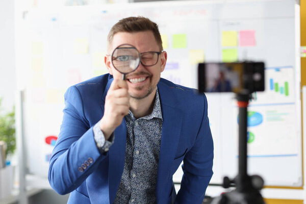 Male blogger looks through magnifying glass at camera