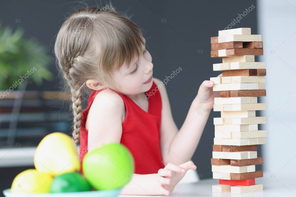 Girl plays and takes out wooden blocks from tower