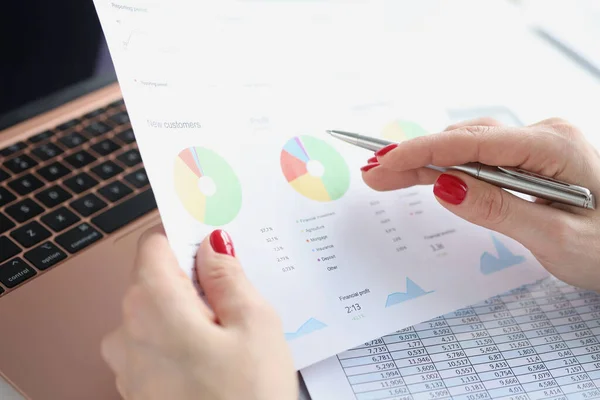 Female hand holds business charts with commercial indicators and pen at workplace — Stock fotografie