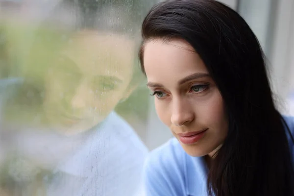 Triste mujer cansada mira por la ventana mientras llueve de cerca — Foto de Stock