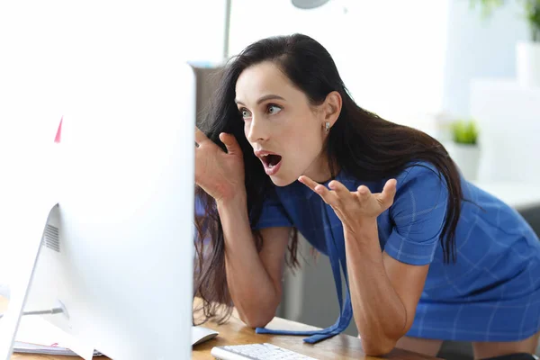 Shocked woman sits at table and looks at computer screen eyes widening in horror — Stock Photo, Image