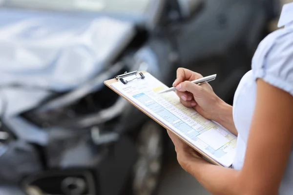 保険募集人は、書類に記入して破損した自動車の点検を行います — ストック写真