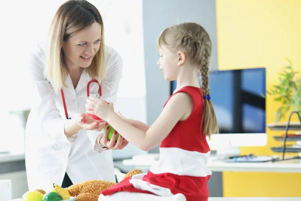 Vrouwelijke arts geeft klein kind appel in de kliniek — Stockfoto