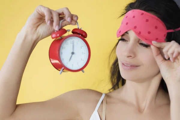 Mujer levantando la máscara del sueño de los ojos y mirando el despertador rojo — Foto de Stock