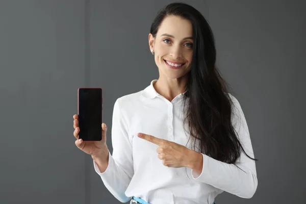 Junge Frau hält Handy in der Hand und zeigt mit Zeigefinger darauf — Stockfoto