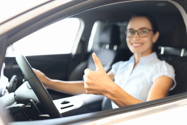 女性は車の車輪の後ろに座って親指を近くに示す — ストック写真