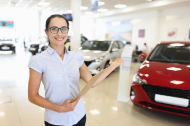 Elinde dosya olan kadın satıcı galeride yeni bir araba gösteriyor.