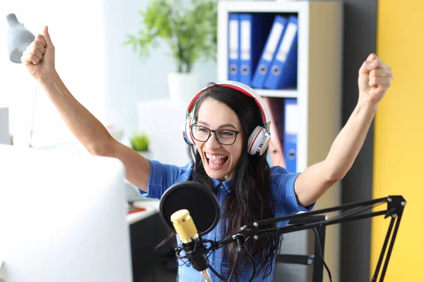 Улыбающаяся женщина в наушниках радуется перед микрофоном на радиостанции — стоковое фото