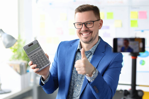 Улыбающийся блогер бизнесмен держит калькулятор и записывает обучающие видео о доходах