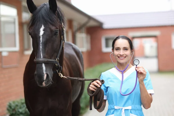 Женщина-ветеринар держит стетоскоп и стоит рядом с лошадью крупным планом — стоковое фото