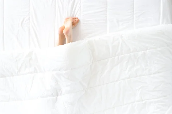 Vrouwen benen uitsteken van onder dekens in bed — Stockfoto