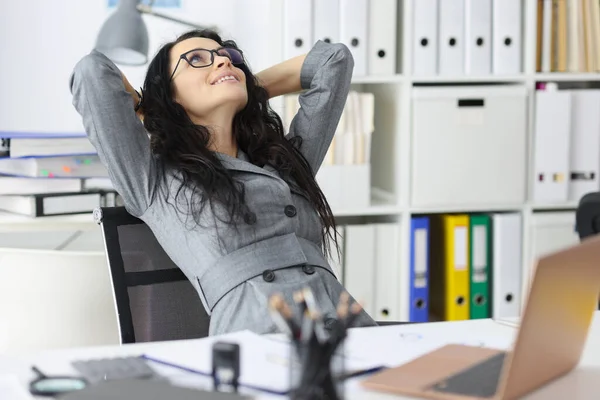 Happy contented woman resting in office sits with laptop and holds hands behind head closeup — Stock Photo, Image