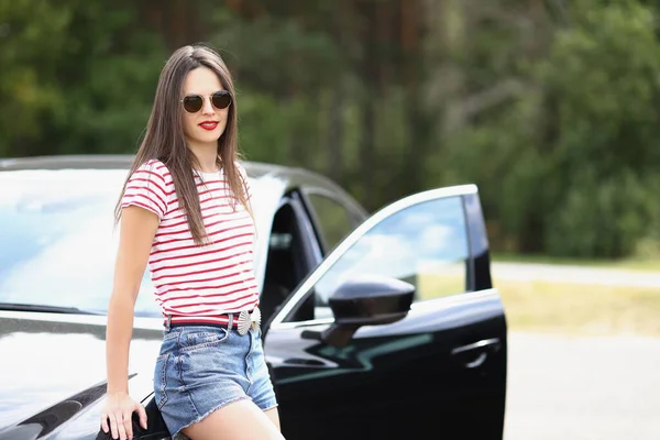 Mulher de calções jeans posando perto de carro preto — Fotografia de Stock