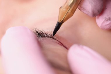 Güzellik salonunda müşteriye göz kapağı dövmesi yapan kalıcı bir makyöz.