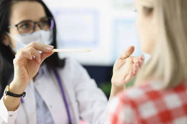 Kvinnlig läkare undersöker halsen på patienten med trä spatel närbild — Stockfoto