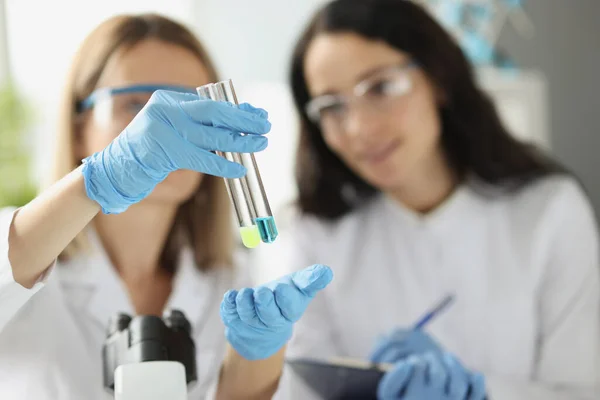 Mulher cientista químico mostrando tubos de ensaio com líquido azul e amarelo em close up laboratório — Fotografia de Stock