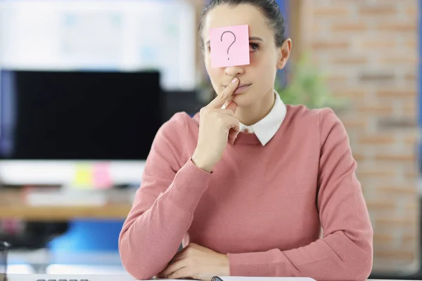 Pensive mladá žena sedí u stolu s nálepkou s otazníkem na čele — Stock fotografie