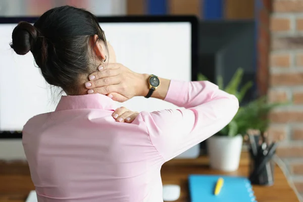 若いです女性座っていますコンピュータと保持彼女の痛み首とともに彼女の手バックビュー — ストック写真