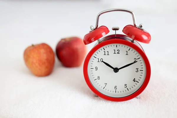 Red alarm clock standing on white towel near apple closeup — Stock Photo, Image