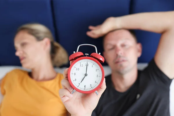 Schläfriger Mann und Frau liegen im Bett und halten roten Wecker in Nahaufnahme — Stockfoto