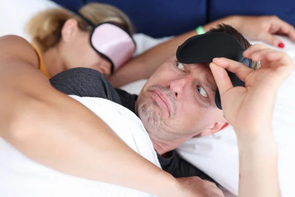 Homem surpreso levantando sua máscara de sono e olhando para a mulher abraçando-o no quarto — Fotografia de Stock