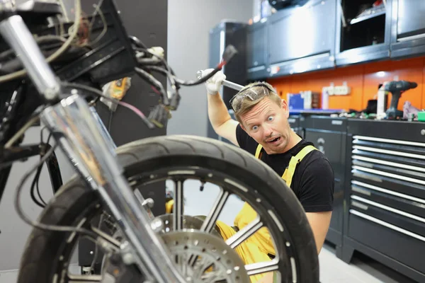 Здивований чоловік ремонтант подряпає голову за допомогою перемикача і дивиться на мотоцикл — стокове фото