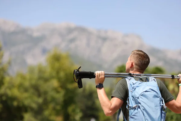 Młody człowiek stoi na szczycie góry i trzyma kije nordic walking — Zdjęcie stockowe