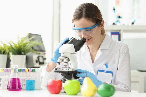 Mujer científica trabajando en microscopio y analizando panal de frutas — Foto de Stock
