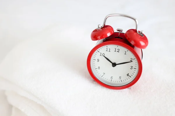Relógio de alarme vermelho fica em closeup toalha branca — Fotografia de Stock