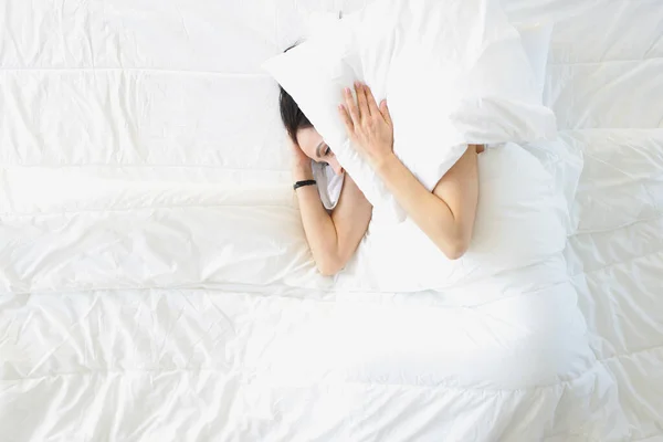 Молода Жінка Лежить Білому Ліжку Прикриває Вуха Видом Зверху Подушкою — стокове фото
