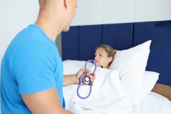 Dokter zit op patiëntenbed en houdt stethoscoop in zijn handen — Stockfoto